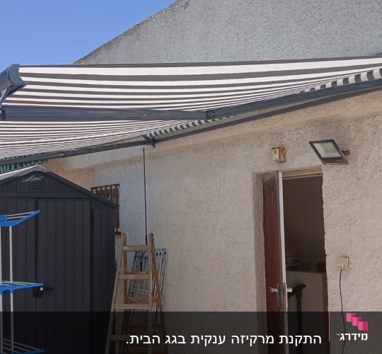 סוכך מפוספס מותקן על קיר חיצוני ליד מחסן